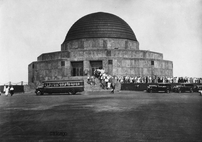 long line waits to get into the Adler Planetarium in its opening day. The building is curved with a dome on top.